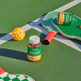 Cordyceps Mushroom Gummies (60 Count) jar alongside a pickleball racket and yellow ball, highlighting energy-boosting gummies in a sports setting.