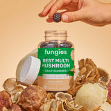 Hand holding a berry over a bottle labeled Best Multi Mushroom Gummies, highlighting the product's focus on wellness with seven functional mushrooms.