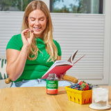 Lion's Mane Mushroom Gummies (60 Count) on a table beside a basket of strawberries and blueberries, with a woman holding a berry nearby.