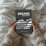 Person holding 'Dreams Remembered' dream logbook on a cozy bed.